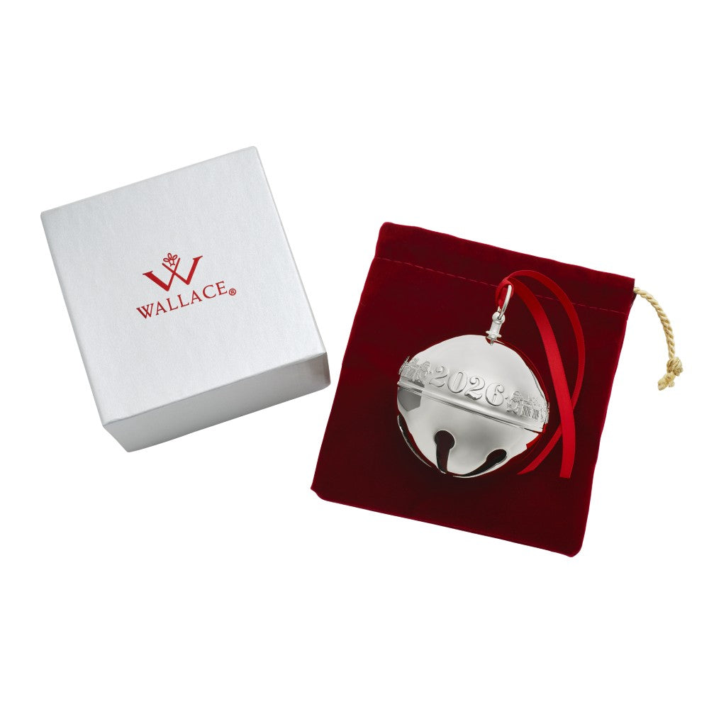 A silver metallic Christmas bell ornament engraved with '2026 CHILE' and hanging from a red ribbon, displayed next to a red velvet pouch and a white Wallace gift box on a white background.