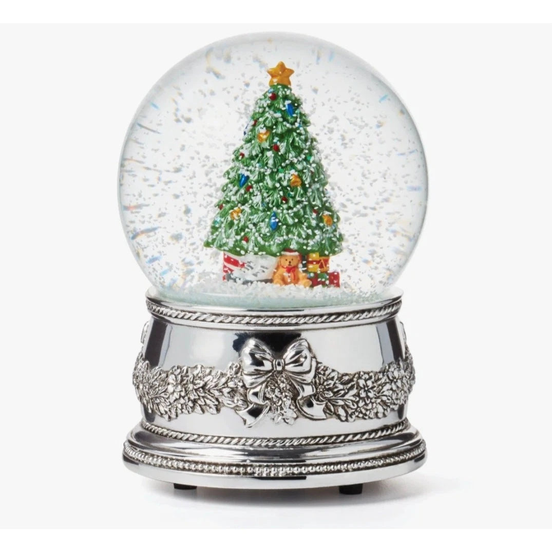 A Christmas-themed snow globe music box featuring a green decorated tree, colorful ornaments, gifts, and falling snow inside a clear globe on an ornate silver base.