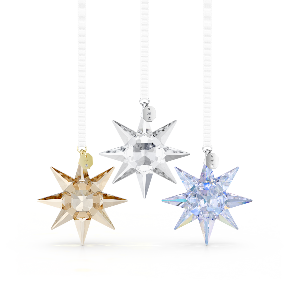Three faceted crystal star ornaments hanging from white ribbons against a clean white background. One ornament is champagne gold, one is clear silver, and one is light blue with an iridescent finish.