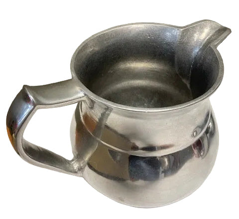 Silver pitcher on a white surface with a neutral background