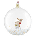 A clear round Christmas ornament with a red hanging ribbon, featuring a small reindeer figurine inside a transparent globe filled with white glitter and gold flecks.